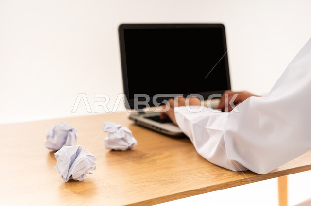 مهنة و عمل مكتبي إداري, دمج التقنية الحديثة و المتطورة مع العمل, اتلاف التقرير الشهري, بورتريه مقرب لأيدي رجل عربي خليجي عماني يرتدي الدشداشة يعمل على جهاز اللابتوب المحمول, خلفية بيضاء