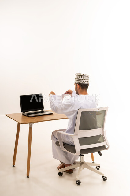 عدم الموافقة على خطة عمل فاشلة, بورتريه من الخلف لرجل عربي خليجي عماني يرتدي الكمه و الدشداشة يجلس على الكرسي أمام طاولة خشبية يقوم بتمزيق الاوراق، صفقة غير ناجحة، اتلاف بعض المعلومات القديمة الغير مهمة, خلفية بيضاء