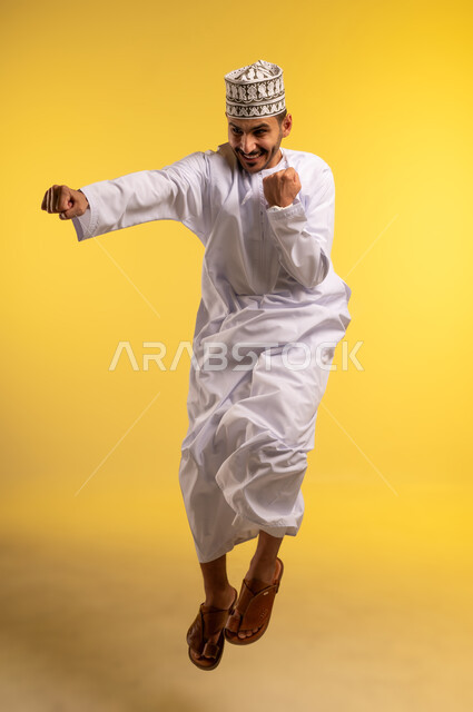 Mastering the art of boxing, practicing self-defense, enhancing bone and joint health, increasing muscle endurance, portrait of an Arab Gulf Omani man wearing a turban and a dishdasha jumping high, raising his fists with gestures of strength, full-length body image, yellow background