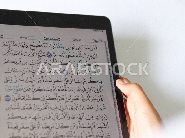 استخدام جهاز تقني الكتروني حديث لقراءة المصحف الشريف، تلاوة القرآن الكريم، صورة مقربة ليدين إمرأة عربية خليجية سعودية تقوم بتتبع الآيات القرآنية من خلال التابلت المحمول، الاجتهاد في العبادة والتقرب الى الله، تحفيظ وتفسير كتاب الله