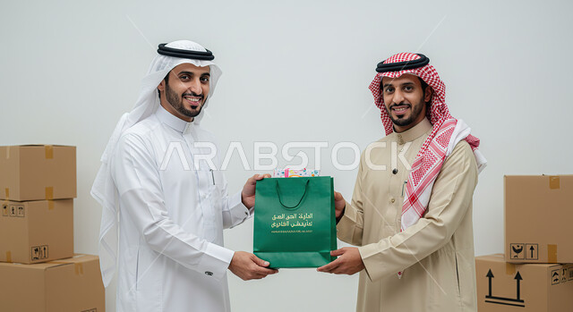 Relying on online purchases, express delivery services, e-shopping concept, ordering products online, portrait of a Saudi Arabian Gulf man wearing traditional thobe and shemagh taking a paper bag from the delivery man, delivering orders to customers easily and quickly, white background