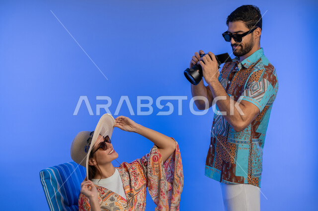 التقاط الصور التذكارية, بورتريه لشاب عربي خليجي سعودي يرتدي الزي الكاجوال يقوم باستخدام كاميرا فوتوغرافية عالية الدقة, شابة اماراتية ترتدي قبعة  من القش تستمتع بجلسة تصوير في إحدى المناطق السياحية, قضاء أوقات ممتعه بالعطلة الصيفية, خلفية زرقاء
