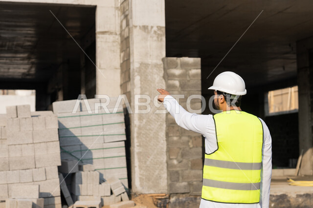 الاشارة الى شيء ما، مهنة هندسية شبابية، مهندس عربي خليجي اماراتي يرتدي الكندورة والسترة وخوذة الحماية يعمل في القطاع الهندسي في الامارات العربية المتحدة، الاشرف على عمليات البناء، مفهوم ادارة المشاريع الهندسية والانشاءات، دراسة المخطط والمشروع على ارض الواقع