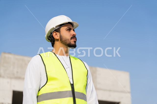 وظيفة ومهنة هندسية شبابية، مهندس عربي خليجي اماراتي يرتدي الكندورة والسترة وخوذة الحماية يعمل في القطاع الهندسي في الامارات العربية المتحدة، الاشرف على عمليات البناء، مفهوم ادارة المشاريع الهندسية والانشاءات، دراسة المخطط والمشروع على ارض الواقع