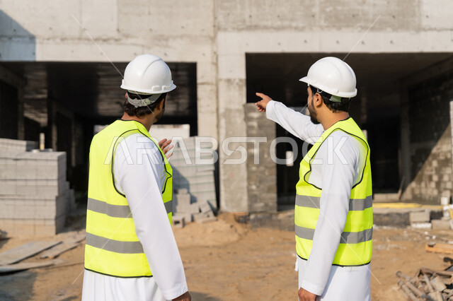 دراسة المخطط والمشروع على ارض الواقع، مهنة ووظيفة هندسية شبابية، مهندسان عربيان خليجيان اماراتيان يرتديان الكندورة والسترة وخوذة الحماية يعملان في القطاع الهندسي في الامارات، مراقبة ومتابعة عمليات البناء، مفهوم ادارة المشاريع الهندسية والانشاءات