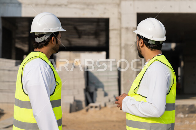 دراسة المخطط والمشروع على ارض الواقع، مهنة ووظيفة هندسية شبابية، مهندسان عربيان خليجيان اماراتيان يرتديان الكندورة والسترة وخوذة الحماية يعملان في القطاع الهندسي في الامارات، مراقبة ومتابعة عمليات البناء، مفهوم ادارة المشاريع الهندسية والانشاءات