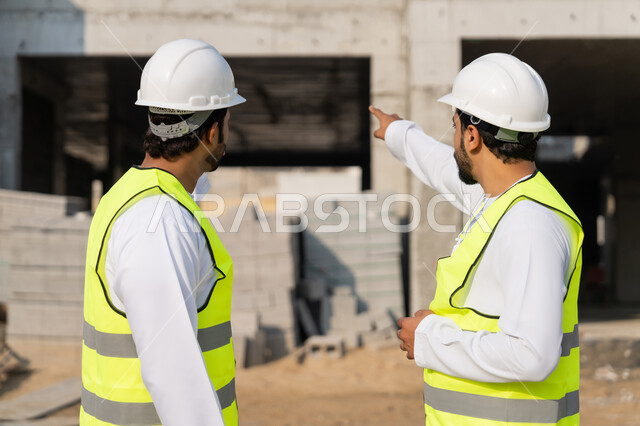 دراسة المخطط والمشروع على ارض الواقع، مهنة ووظيفة هندسية شبابية، مهندسان عربيان خليجيان اماراتيان يرتديان الكندورة والسترة وخوذة الحماية يعملان في القطاع الهندسي في الامارات، مراقبة ومتابعة عمليات البناء، مفهوم ادارة المشاريع الهندسية والانشاءات