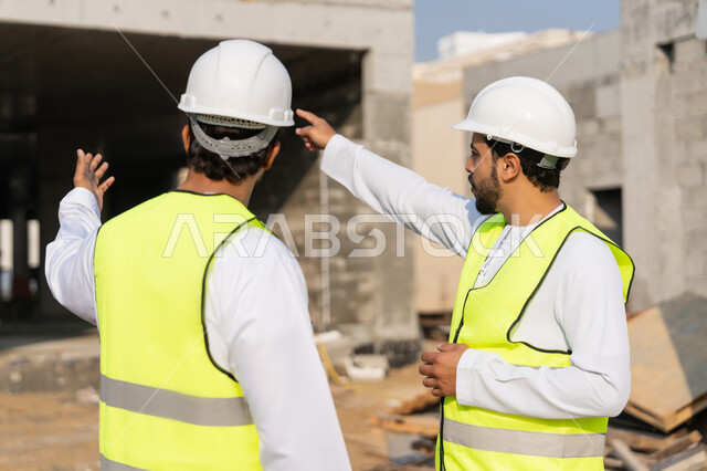 دراسة المخطط والمشروع على ارض الواقع، مهنة ووظيفة هندسية شبابية، مهندسان عربيان خليجيان اماراتيان يرتديان الكندورة والسترة وخوذة الحماية يعملان في القطاع الهندسي في الامارات، مراقبة ومتابعة عمليات البناء، مفهوم ادارة المشاريع الهندسية والانشاءات