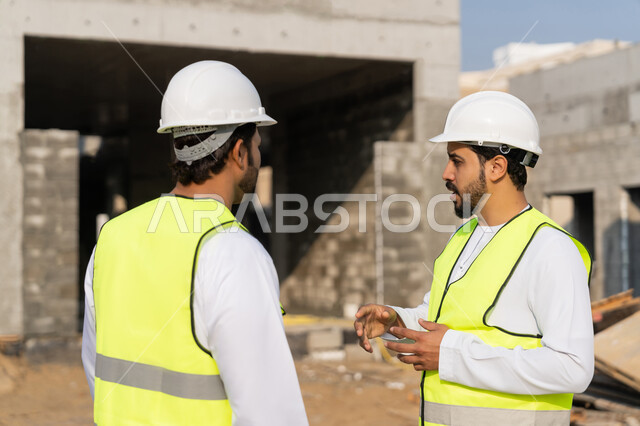 دراسة المخطط والمشروع على ارض الواقع، مهنة ووظيفة هندسية شبابية، مهندسان عربيان خليجيان اماراتيان يرتديان الكندورة والسترة وخوذة الحماية يعملان في القطاع الهندسي في الامارات، مراقبة ومتابعة عمليات البناء، مفهوم ادارة المشاريع الهندسية والانشاءات