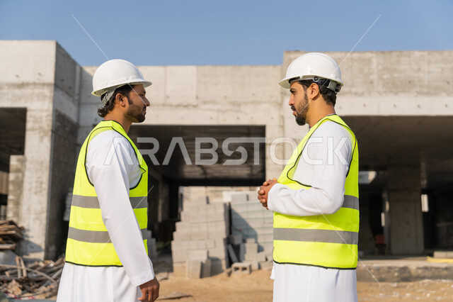 دراسة المخطط والمشروع على ارض الواقع، مهنة ووظيفة هندسية شبابية، مهندسان عربيان خليجيان اماراتيان يرتديان الكندورة والسترة وخوذة الحماية يعملان في القطاع الهندسي في الامارات، مراقبة ومتابعة عمليات البناء، مفهوم ادارة المشاريع الهندسية والانشاءات