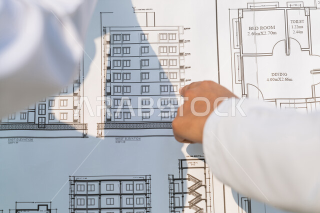 دراسة المخطط والمشروع على ارض الواقع، وظيفة هندسية شبابية، صورة مقربة من الخلف لمهندسان عربيان خليجيان اماراتيان يرتديان الكندورة والسترة يشيران الى المخطط، العمل في القطاع الهندسي في الامارات، مراقبة ومتابعة عمليات البناء، مفهوم ادارة المشاريع الهندسية والانشاءات