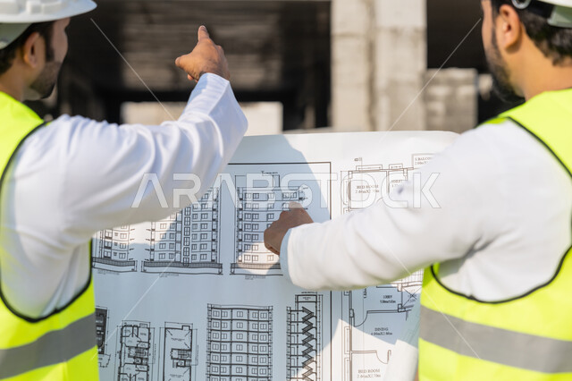 دراسة المخطط والمشروع على ارض الواقع، مهنة ووظيفة هندسية شبابية، مهندسان عربيان خليجيان اماراتيان يرتديان الكندورة والسترة وخوذة الحماية يعملان في القطاع الهندسي في الامارات، مراقبة ومتابعة عمليات البناء، مفهوم ادارة المشاريع الهندسية والانشاءات