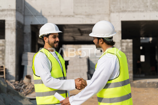 إيماءات المصافحة والترحيب والاستقبال, مفهوم التعاون والعمل المشترك, مهندسان عربيان خليجيان اماراتيان يرتديان الخوذة وسترة الحماية يقومان بالتصافح والاتفاق على الخطط والمشاريع الهندسية في موقع العمل, الإنشاءات المعمارية في الأراضي الاماراتية