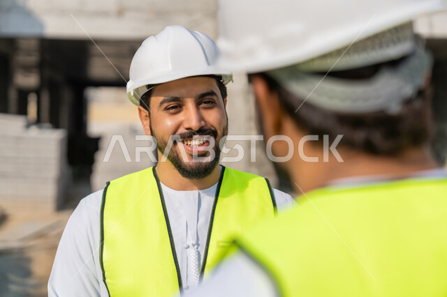 تبادل المعلومات والخبرة، دراسة المخطط والمشروع على ارض الواقع، وظيفة هندسية شبابية، مهندسان عربيان خليجيان اماراتيان يرتديان الكندورة والسترة وخوذة الحماية يعملان في القطاع الهندسي في الامارات، مراقبة ومتابعة عمليات البناء، مفهوم ادارة المشاريع الهندسية والانشاءات