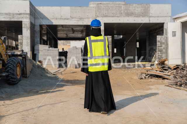 الاشراف على أعمال البناء وصب الخرسانات ووضع الأساسات الأولية، مهنة ووظيفة نسائية، صورة من الخلف لمهندسة عربية خليجية سعودية محجبة ترتدي السترة والخوذة تقوم بمتابعة مبنى قيد الإنشاء والتشييد، مفهوم الهندسة الانشائية والمعمارية، إمرأة اماراتية تقف في موقع البناء