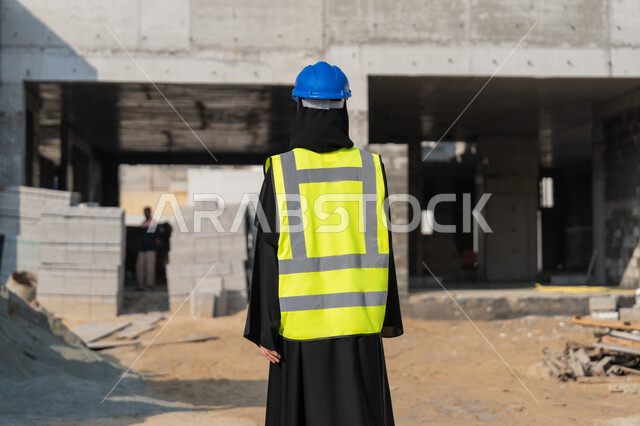 الاشراف على أعمال البناء وصب الخرسانات ووضع الأساسات الأولية، مهنة ووظيفة نسائية، صورة من الخلف لمهندسة عربية خليجية سعودية محجبة ترتدي السترة والخوذة تقوم بمتابعة مبنى قيد الإنشاء والتشييد، مفهوم الهندسة الانشائية والمعمارية، إمرأة اماراتية تقف في موقع البناء
