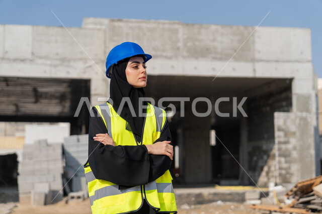 مراقبة أعمال البناء وصب الخرسانات ووضع الأساسات الأولية، مهنة ووظيفة نسائية، مهندسة عربية خليجية سعودية ترتدي السترة والخوذة تقوم بالاشراف على مبنى قيد الإنشاء والتشييد، مفهوم الهندسة الانشائية والمعمارية، إمرأة اماراتية تقف في موقع البناء بأيدي متقاطعة