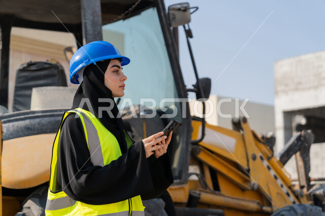 استخدام جهاز تقني حديث، مهنة ووظيفة نسائية، إمرأة عربية خليجية سعودية ترتدي السترة والخوذة تقوم بالاشراف على مبنى قيد الإنشاء والتشييد، مفهوم الهندسة الانشائية والمعمارية، مهندسة اماراتية تمسك بيدها الهاتف المحمول، أعمال البناء وصب الخرسانات ووضع الأساسات الأولية