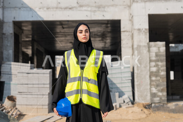 متابعة أعمال البناء وصب الخرسانات ووضع الأساسات الأولية، مهنة ووظيفة نسائية، مهندسة عربية خليجية سعودية ترتدي السترة تمسك الخوذة تقوم بالاشراف على مبنى قيد الإنشاء والتشييد، مفهوم الهندسة الانشائية والمعمارية، إمرأة اماراتية تقف في موقع البناء