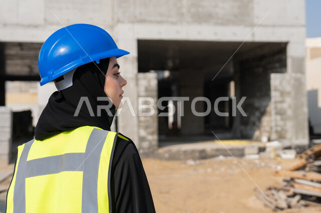 مفهوم الهندسة الانشائية والمعمارية، إمرأة اماراتية تقف في موقع البناء، الاشراف على أعمال البناء وصب الخرسانات ووضع الأساسات الأولية، مهنة ووظيفة نسائية، صورة مقربة لمهندسة عربية خليجية سعودية محجبة ترتدي السترة والخوذة تقوم بمتابعة مبنى قيد الإنشاء والتشييد