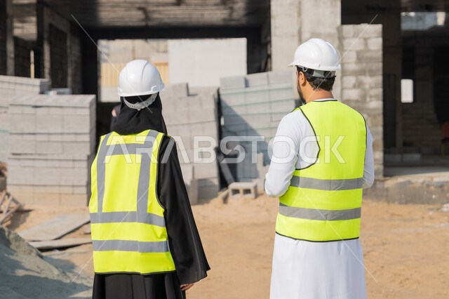 الاشراف والمتابعة على المشاريع الهندسية والانشاءات، دراسة المخطط والمشروع على ارض الواقع، مهنة ووظيفة هندسية، مهندس عربي خليجي اماراتي يرتدي الكندورة والسترة وخوذة الحماية يعمل مع زميلته في القطاع الهندسي في الامارات العربية المتحدة، مراقبة وادارة عمليات البناء