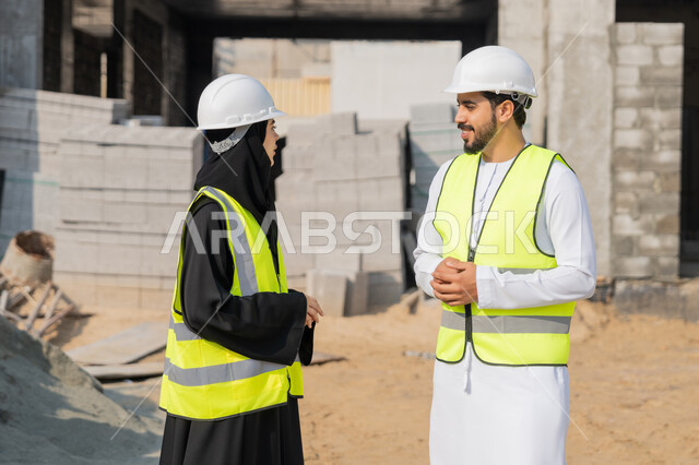 الاشراف والمتابعة على المشاريع الهندسية والانشاءات، دراسة المخطط والمشروع على ارض الواقع، مهنة ووظيفة هندسية، مهندس عربي خليجي اماراتي يرتدي الكندورة والسترة وخوذة الحماية يعمل مع زميلته في القطاع الهندسي في الامارات العربية المتحدة، مراقبة وادارة عمليات البناء