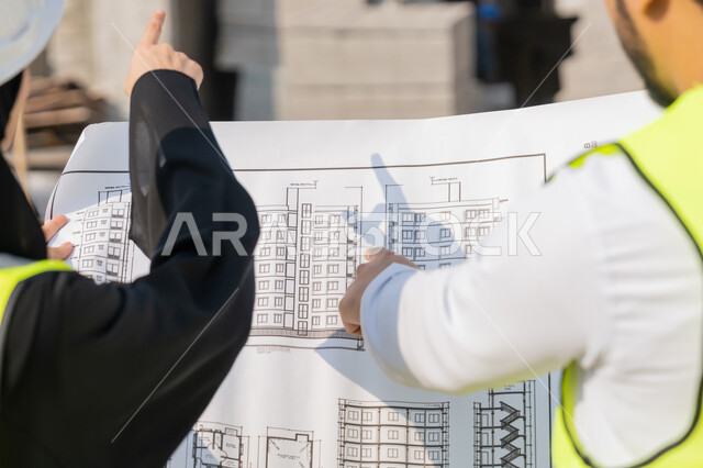 المتابعة والاشراف على المشاريع الهندسية والانشاءات، دراسة المخطط والمشروع على ارض الواقع، مهنة ووظيفة هندسية، مهندس عربي خليجي اماراتي يرتدي الكندورة والسترة وخوذة الحماية يعمل مع زميلته في القطاع الهندسي في الامارات العربية المتحدة، مراقبة وادارة عمليات البناء