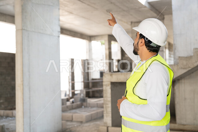 الاشارة الى شيء ما، مهنة هندسية شبابية، مهندس عربي خليجي اماراتي يرتدي الكندورة والسترة وخوذة الحماية يعمل في القطاع الهندسي في الامارات العربية المتحدة، الاشرف على عمليات البناء، مفهوم ادارة المشاريع الهندسية والانشاءات، دراسة المخطط والمشروع على ارض الواقع