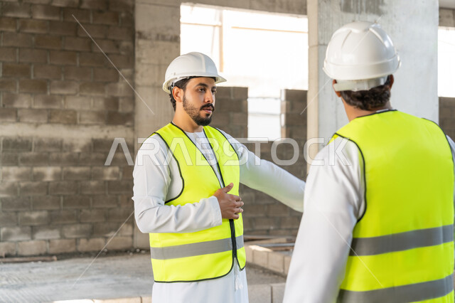 مراقبة ومتابعة عمليات البناء، مفهوم ادارة المشاريع الهندسية والانشاءات، دراسة المخطط والمشروع على ارض الواقع، مهنة ووظيفة هندسية شبابية، مهندسان عربيان خليجيان اماراتيان يرتديان الكندورة والسترة وخوذة الحماية يعملان في القطاع الهندسي في الامارات