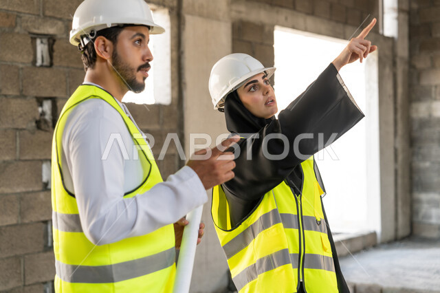 ادارة المشاريع الهندسية والانشاءات، دراسة المخطط والمشروع على ارض الواقع، مهنة ووظيفة هندسية، مهندس عربي خليجي اماراتي يرتدي الكندورة والسترة وخوذة الحماية يعمل مع زميلته في القطاع الهندسي في الامارات العربية المتحدة، مراقبة ومتابعة عمليات البناء