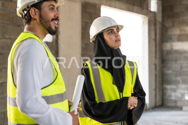 المتابعة والاشراف على المشاريع الهندسية والانشاءات، دراسة المخطط والمشروع على ارض الواقع، مهنة ووظيفة هندسية، مهندس عربي خليجي اماراتي يرتدي الكندورة والسترة وخوذة الحماية يعمل مع زميلته في القطاع الهندسي في الامارات العربية المتحدة، مراقبة وادارة عمليات البناء