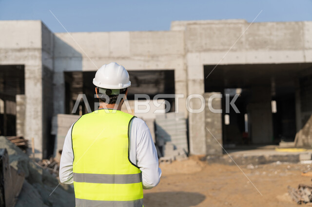 مهنة ووظيفة هندسية شبابية، مهندس عربي خليجي اماراتي يرتدي الكندورة والسترة وخوذة الحماية يعمل في القطاع الهندسي في الامارات العربية المتحدة، الاشرف على عمليات البناء، مفهوم ادارة المشاريع الهندسية والانشاءات، دراسة المخطط والمشروع على ارض الواقع