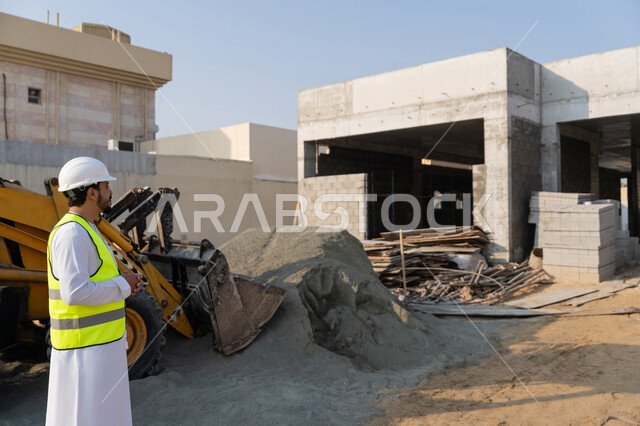 مهنة ووظيفة هندسية شبابية، مهندس عربي خليجي اماراتي يرتدي الكندورة والسترة وخوذة الحماية يعمل في القطاع الهندسي في الامارات العربية المتحدة، الاشرف على عمليات البناء، مفهوم ادارة المشاريع الهندسية والانشاءات، دراسة المخطط والمشروع على ارض الواقع