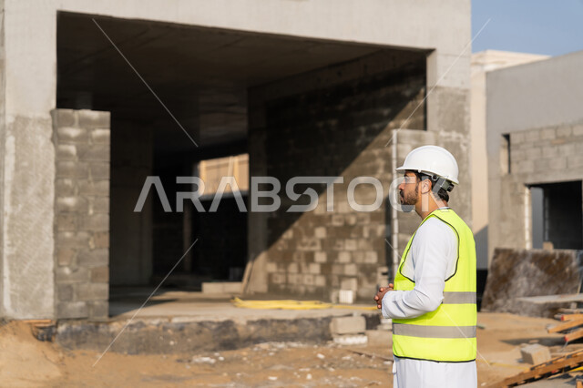 مفهوم ادارة المشاريع الهندسية والانشاءات، دراسة المخطط والمشروع على ارض الواقع، مهنة ووظيفة هندسية شبابية، مهندس عربي خليجي اماراتي يرتدي الكندورة والسترة وخوذة الحماية يعمل في القطاع الهندسي في الامارات العربية المتحدة، الاشرف على عمليات البناء