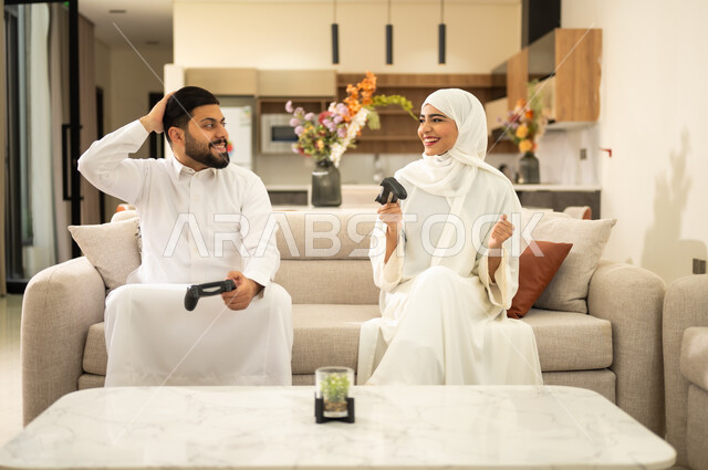 العاب العالم الافتراضى ، ايماءات الفوز والخسارة ، الاستمتاع بالتقنيات والتكنولوجيا الحديثة ، زوجان عربيان خليجيان سعوديان يمسكان عصا التحكم ، قضاء اوقات الفراغ السعيدة مع العائلة ، فعاليات عطلة نهاية الأسبوع  .