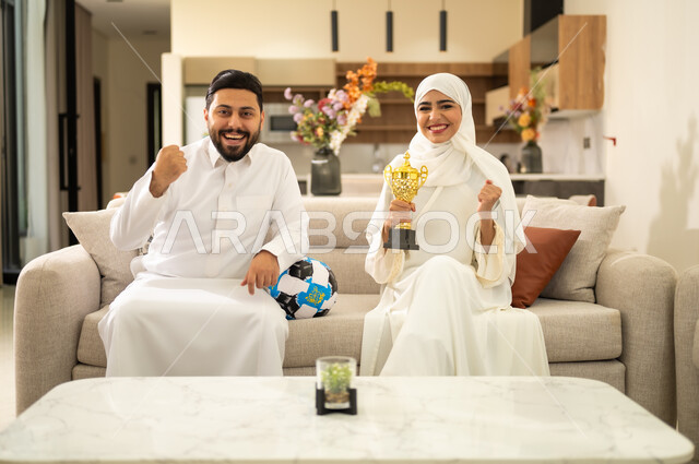 مفهوم الاندماج بمشاهدة الفريق المفضل ، قضاء اوقات الفراغ الممتعة مع الزوجة ، الحماس والتفاعل مع المنتخب ،المباريات والألعاب الرياضية، الحماس بالفوز بالكأس، زوجان عربيان خليجيان سعوديان  يقومان بمشاهدة ومتابعة كرة القدم بتعابير الانتصار.