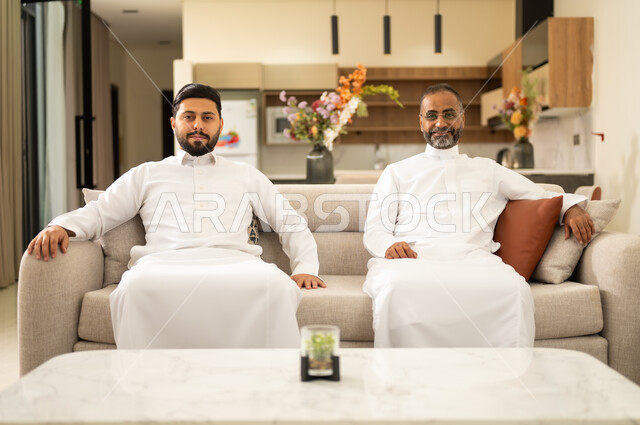 قضاء أوقات مليئه بالحب والموده ، مفهوم الأمان والإستقرار العائلي ، أجواء عائليه سعيده مليئه بالحب والحنان، رجل عربي خليجي سعودي يرتدي الزي التقليدي ويجلس مع ابنه ، ايماءات الفرح والسعاده ، الألفه والمحبه بين الآباء والابناء .