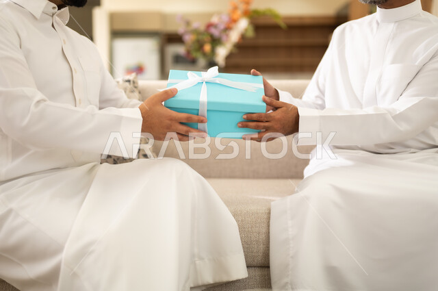حب واحترام الاباء ، مفهوم تقدير وبر الوالدين ، إدخال الفرحة والسرور الى قلب الأب، التربية الصالحة للأبناء, صورة مقربة ليد رجل عربي خليجي سعودي يقدم هدية لوالده في أجواء العيد , إيماءات الفرح و البهجة, تقديم الهدايا فى المناسبات و العيد السعيد .