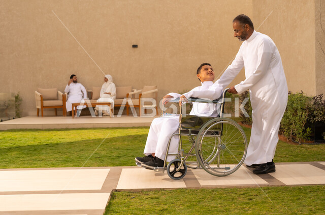 الضعف في القدرة الحركية ، مساعدة مرضى ذوي الهمم على التنقل بسهولة ، قضاء الوقت في المنتزه مع العائلة ، صورة من الجانب لولد عربي خليجي سعودي مقعد يجلس على كرسي متحرك ،  دعم المجتمع لذوي الاحتياجات الخاصه ، الاخلاص والعطف بين افراد الاسرة  ،  خلفية الطبيعة.