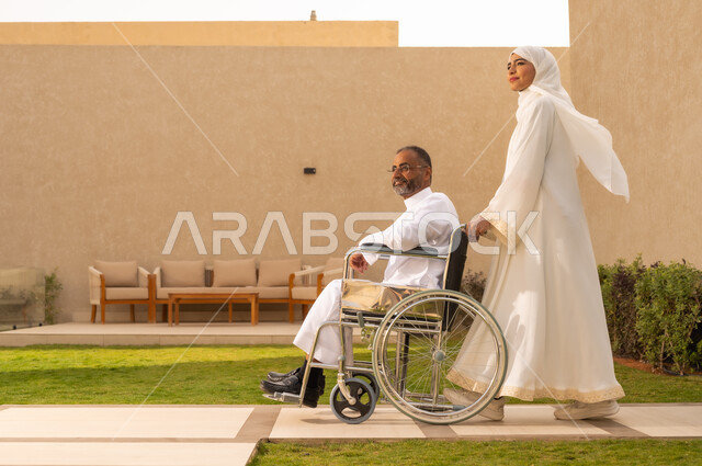نمط حياة ذوي الإعاقة الحركية ، شعور ذوي الهمم بالراحه والطمأنينه ، رجل مقعد يجلس على كرسي متحرك، امرأة عربية خليجية سعودية ترتدي العباءة والحجاب، تساعد زوجها على التنقل والحركة  ،  النظر الى شئ ما بايماءات الفرح والسرور ، خلفية الطبيعة.