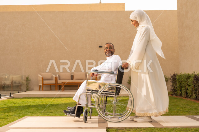 ايماءات الحنان و العطف والشعور بالمحبة  ، تأمين أدوات ومعدات لمساعدة المرضي ، رجل مقعد يجلس على كرسي متحرك، امرأة عربية خليجية سعودية ترتدي العباءة والحجاب، تنظر الى زوجها  بايماءات الحب والسرور ، تساعد زوجها على التنقل والحركة  ، خلفية الطبيعة.