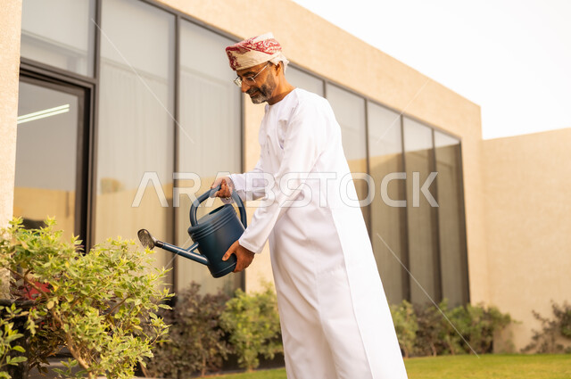 الوعي البيئي وأهمية الحفاظ على الطبيعة ، رجل عربي خليجي عماني يقوم باستخدام وعاء السقي في ري النباتات ، استخدام مرش المياة ، قضاء الوقت الممتع في إحدى الشاليهات ، الاعتناء والاهتمام بالنباتات الخضراء ، خلفية الطبيعة .