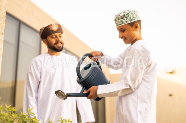 مفهوم النظافة والاهتمام بحديقة المنزل ، رجل عربي خليجي عماني يقضي وقت ممتع مع إبنه في ري النباتات بإستخدام وعاء السقي ، فعاليات وأجواء ترفيهية ، ايماءات السعادة على وجوههم ، الاجواء الطبيعية الجميلة ، المتعة و التسليه والترفيه ، قضاء الوقت الممتع في إحدى الشاليهات .