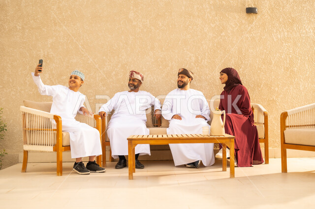 مفهوم الأمان والإستقرار العائلي، توثيق اللحظات العائلية الممتعة  بإيماءات السعادة والفرح، عائلة عربية خليجية عمانية تلتقط صورة تذكارية من خلال الهاتف المحمول، المحافظة على الترابط الأسري، قضاء الاوقات الممتعة مع الاهل .