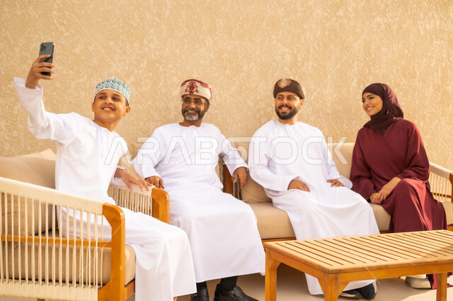 استخدام الجوال لالتقاط صور سيلفي تذكارية ، عائلة عربيه خليجية عمانية سعيدة تقوم بتوثيق اللحظات الممتعة بإيماءات السعادة والفرح, فرحة الأبناء بقضاء وقت ممتع مع الأهل .