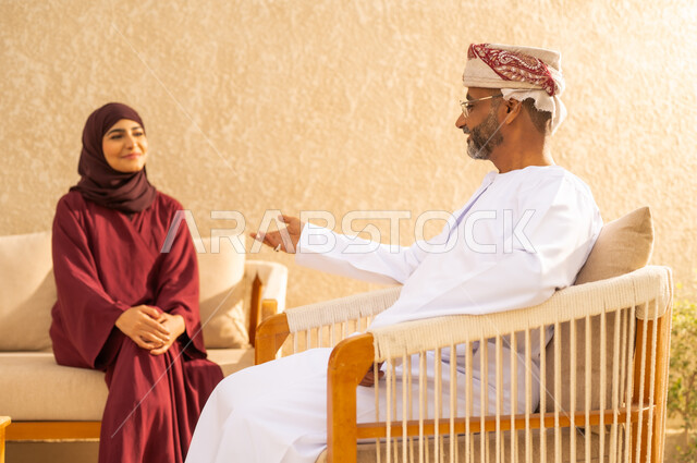 التفاهم بين الزوجين ، مفهوم السعادة الزوجية ، رجل عربي خليجي عماني يرتدي الدشداشة والكمة ، يجلس مع زوجتة و يتبادلان أطراف الحديث بانسجام ، اجواء عائلية دافئة ، الشعور بالحب والامان ، قضاء أوقات ممتعة مع الزوجة .