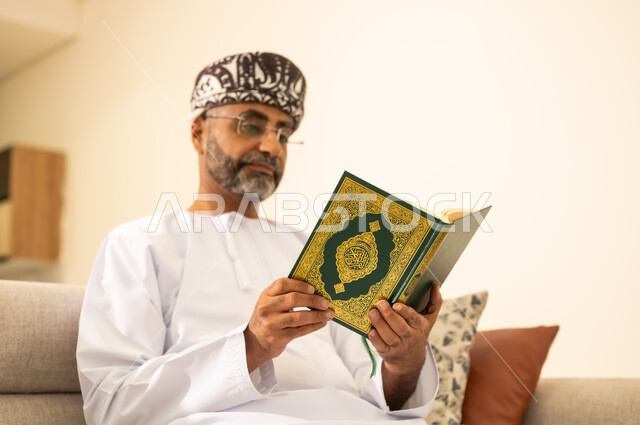 ايماءات الخشوع والطمأنينة، الاجتهاد في العبادة، تلاوة وقراءة القرآن الكريم وتدبر معانيه، صورة مقربة لرجل عربي خليجي عماني يرتدي الدشداشة والعمامة يحمل بيده المصحف الشريف ، الإكثار من ذكر الله تعالى، التقرب الى الله  .