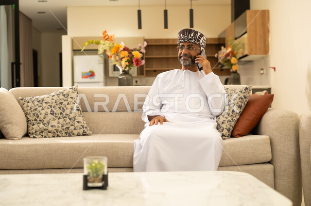 Gestures of happiness and joy, communicating with family and friends, integrating modern technology into daily life. A close-up image of an Arab Gulf man wearing a dishdasha and a kummah making a mobile phone call.
