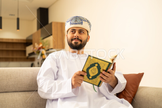 التقرب الى الله، تدبر آيات القران الكريم، الشعور بالخشوع والطمأنينة ، الاجتهاد في العبادة، رجل عربي خليجي عماني يرتدي الدشداشة والعمامة يحمل بيده المصحف الشريف وينظر الى شئ ما ، الإكثار من ذكر الله تعالى .