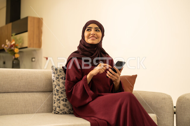 E-marketing, internet browsing, a Saudi Arabian Gulf woman wearing an abaya and hijab, holding a mobile phone and looking at something with happy gestures, an Omani Arabian Gulf woman using modern and advanced devices and technologies, social media.